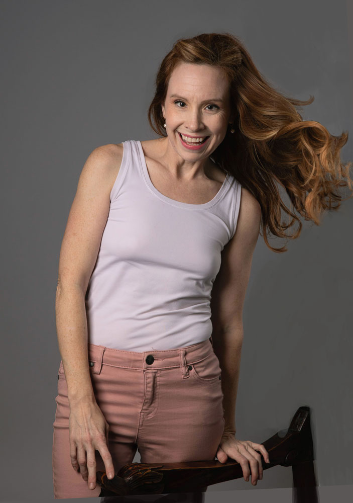 3/4 length portrait of Adrienne Maples in pink jeans and white tank top.