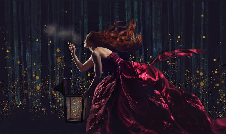 Redheaded woman in red dress flowing behind her as she reaches out to catch fireflys.